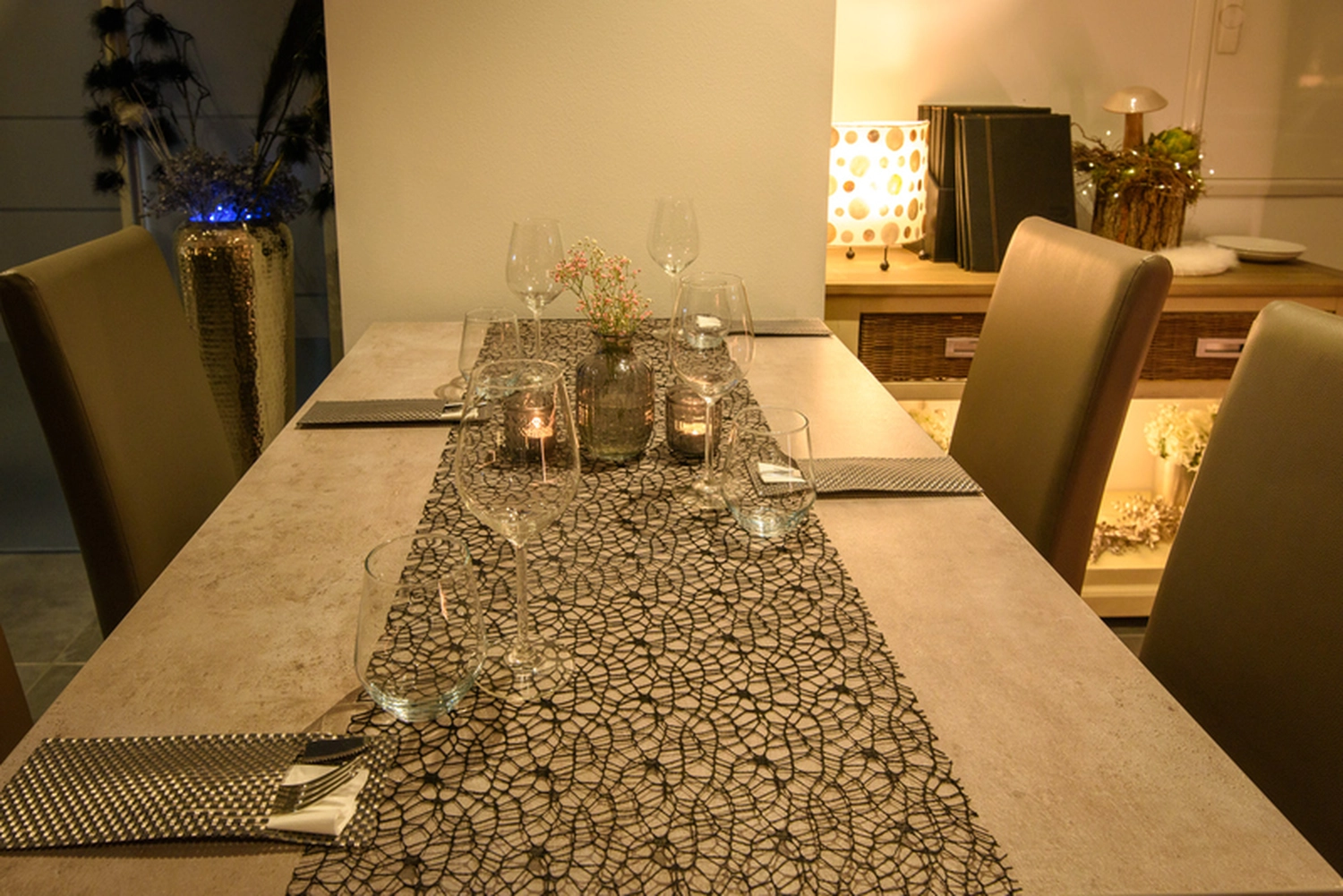 Champions Restaurant und Sportsbar - Genießen Sie frisch zubereitete Speisen, kühle Getränke - Ein Esstisch, gedeckt für ein intimes Abendessen mit Weingläsern, Kerzen und einem kleinen Blumenarrangement in einem gemütlichen, schwach beleuchteten Raum.