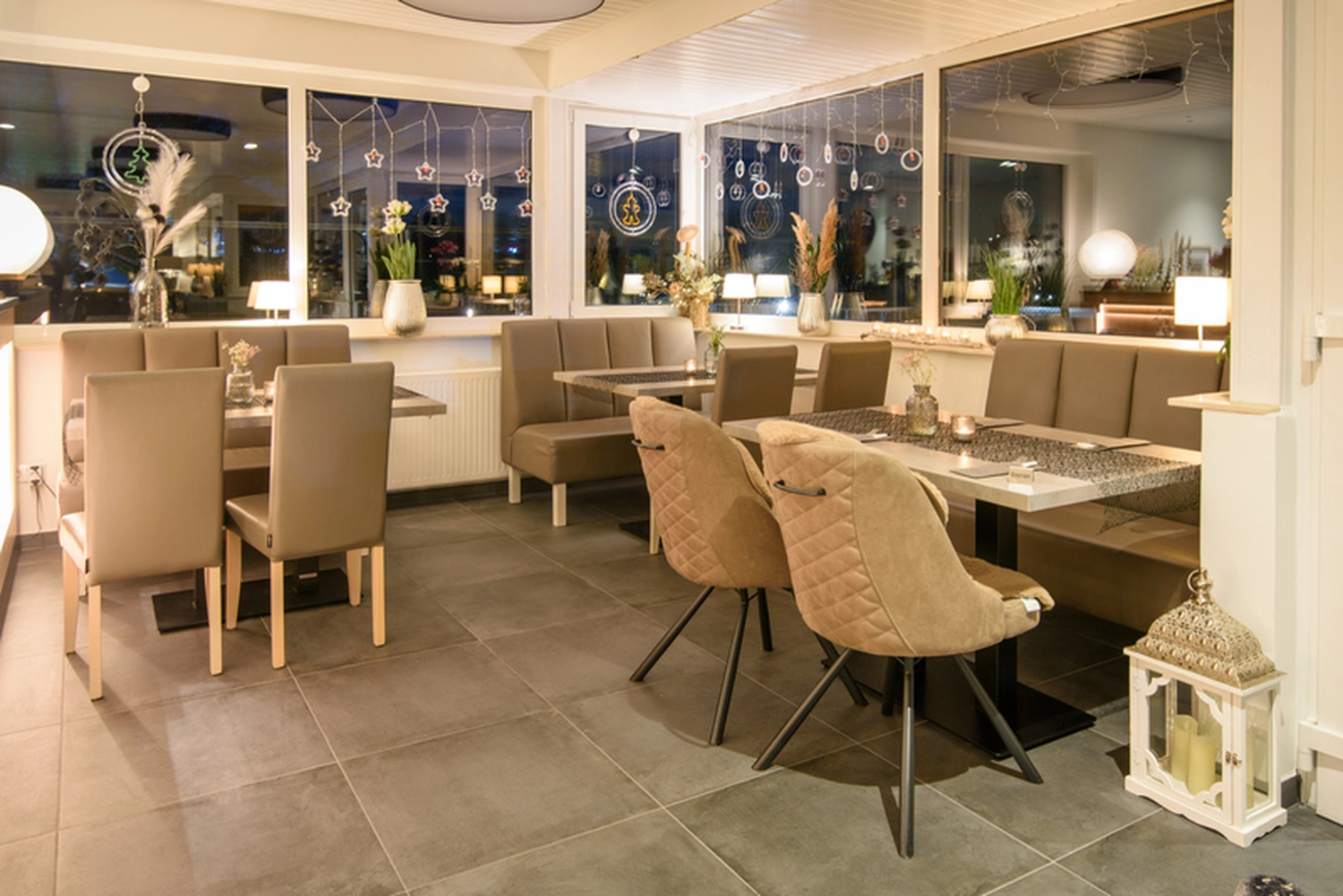 Champions Restaurant und Sportsbar - Genießen Sie frisch zubereitete Speisen, kühle Getränke -  Ein gemütliches Restaurantinterieur mit modernen, braunen Stühlen und Tischen, großen Fenstern und warmer Beleuchtung.